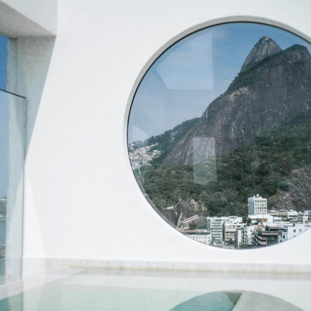 Vista das montanhas e da cidade através de uma grande janela redonda no moderno e branco JANEIRO Hotel.