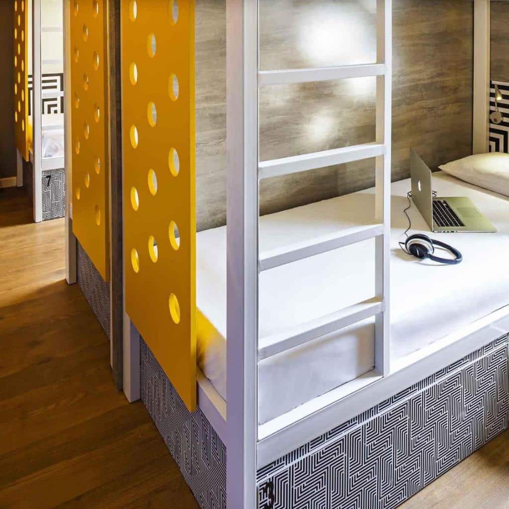 Beliches modernos com divisórias amarelas no ibis budget Rio de Janeiro Centro, além de um laptop e fones de ouvido em uma cama branca.